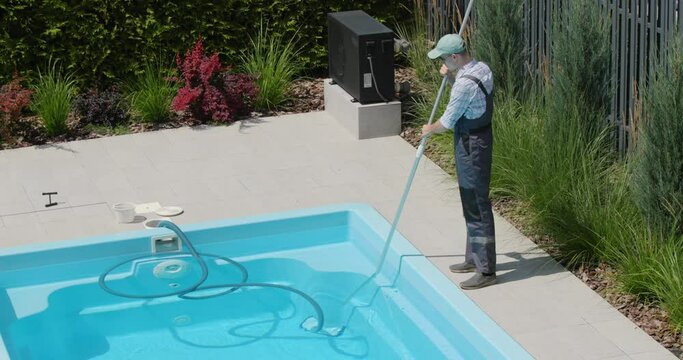 Worker in overalls vacuuming the pool in the backyard of the house. Top view