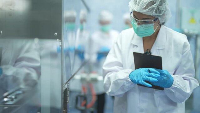 Female factory workers check machine systems at the industrial factory. Women working in clean rooms for beverage and food production. Female worker recording data at the control panel.
