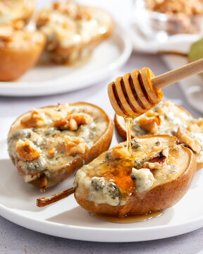 Baked pears with blue cheese, walnuts and honey on white plate and light background