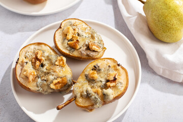 Baked pears with blue cheese, walnuts and honey on white plate and light background