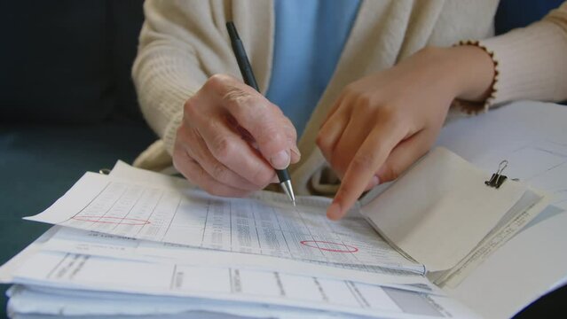 Close up shot of hands of elderly woman making notes in personal expense worksheet with assistant of caregiver while planning budget at home