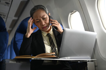 Positive middle aged businesswoman calling business contact during flight