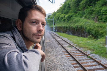 Young man looking out of train window while traveling by railway through Balkans. Male traveler...