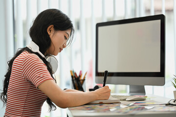 Side view of young woman with wireless headphone writing notes in personal daily, planning workday at desk