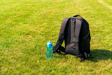 Black backpack and water bottleon the green grass background