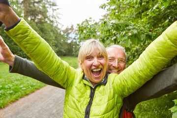 Happy elderly couple wearing jackets hiking in forest