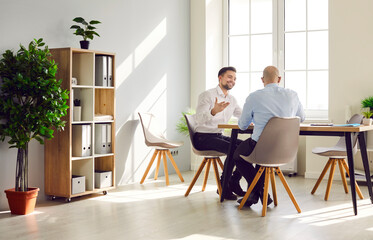 Two business men sitting at the desk of workplace talking and discussing company finance in office. Male company employers considering new projects, analyzing company. Team work concept.