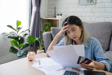 young Asian woman is stressed because she looks at many expense bills and she has no money to pay...