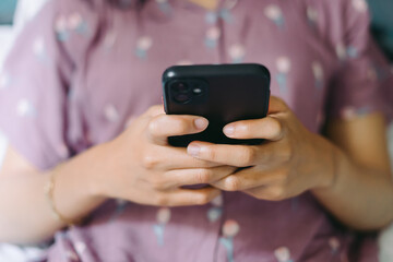 Close up woman hand in pajamas lies on a bed looking at a smartphone screen. Streaming watching leisure concept