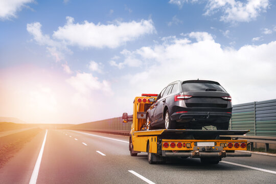 A tow truck on the public road. Tow truck with broken car on country road. Tow truck transporting car on the highway. Car service transportation concept.
