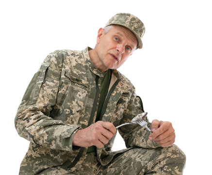 Portrait of Ukraine army soldier sits with a spoon and fork in his hands and demands some food, isolated on white background. Old defender posing in studio.