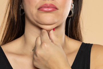Young woman touches her double chin on beige background, closeup. Front view - obrazy, fototapety, plakaty