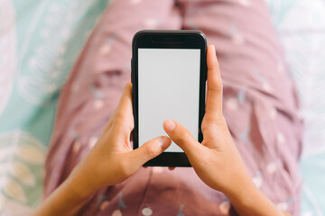 Close up woman hand in pajamas lies on a bed looking at a smartphone with a white screen. Streaming leisure concept