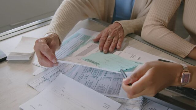 Close up high angle shot of hands of female financial advisor and senior woman discussing bills while planning budget during consultation at home