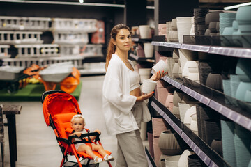 Young woman amateur gardener choosing pots for growing plants in floral and garden supplies store.