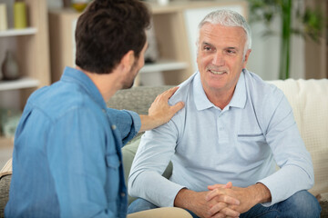 grown son sit on couch relax talking with senior dad