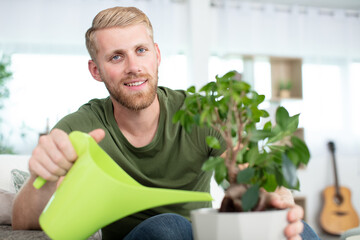 attractive young man on apartment watering plants