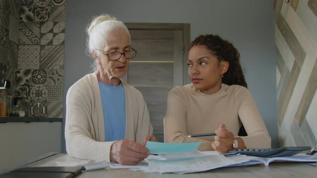 Medium shot of female financial advisor discussing bills with senior woman while giving her at-home consultation about money managementMedium shot of female financial advisor discussing bills with sen