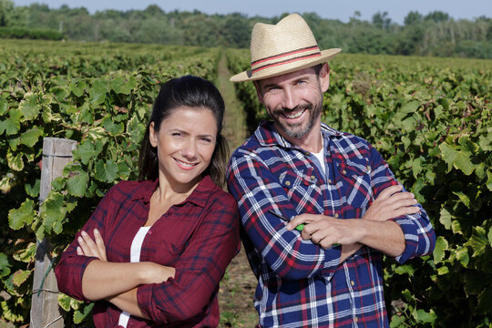 portrait of smiling couple with arms crossed standing at vineyard