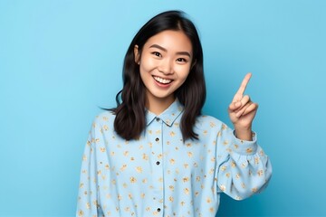 Generative AI : Happy asian woman travel backpacker standing pointing hands to copyspace on blue background Cute asia girl smiling wearing casual jeans shirt and finger pointing to aside for present p - obrazy, fototapety, plakaty