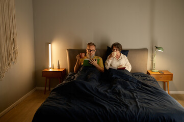 Calm family couple on retirement reading book together in bed