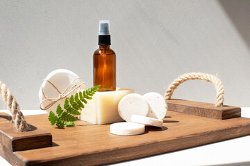 Amber bottle with facial cosmetics on a wooden tray with natural soap bars on the beige concrete...