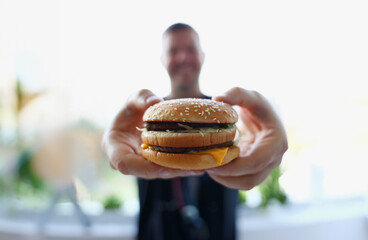 Satisfied young man holding a hamburger in his hands at the office during lunch break food delivery concept