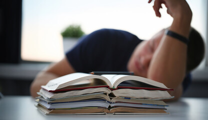 Tired male student at workplace in room taking nap on pile of textbooks. Sleepy man resting during education after sleepless night. Student in despair caused by exam deadline concept