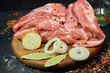 A piece of raw meat and spices lie on a wooden cutting board. Raw food for cooking.