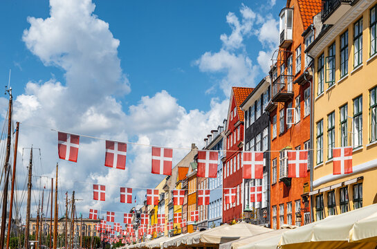 Waving danish flags above touristic street with colorful buildings in Nyhavn, Copenhagen in Denmark.