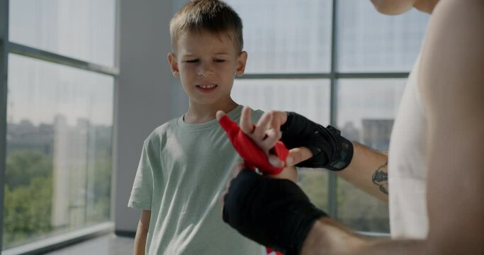 Sportsman father helping child son with hands wrapping preparing for training in gym together. Family workout and active lifestyle concept.