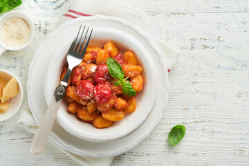 Potato gnocchi. Traditional homemade potato gnocchi with tomato sauce, basil and parmesan cheese on kitchen table on light grey kitchen table background. Traditional Italian food. Top view.