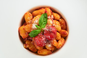 Potato gnocchi. Traditional homemade potato gnocchi with tomato sauce, basil and parmesan cheese on kitchen table on white kitchen table background. Traditional Italian food. Top view.