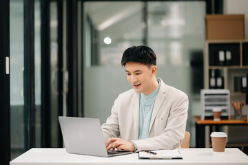 Young Asian business man working at office with laptop, tablet and taking notes on the paper.