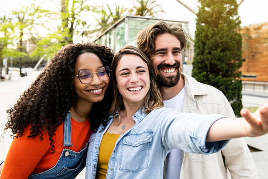 Diverse group of three friends taking a selfie in the street. Cheerful multiracial group of young hipsters taking a picture outside.