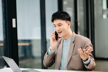 Business asian man Talking on the phone and using a laptop with a smile while sitting at modern office