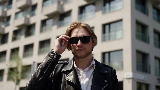 Fashionable man in black glasses in sunny summer light and buildings in the background. Summer mood, slow-motion fashion video. Blonde in sunglasses.