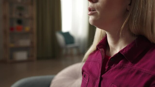 Blonde woman sitting on the sofa, having an asthma attack and using an inhaler, close up shot