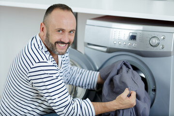 Obraz premium handsome man putting laundry in washing machine