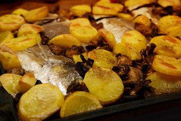 oven grilled sea bream fish with delicious curry sauce served on baking tray, baked potatoes with champignon mushrooms, spices, junk food concept, traditional family party, fish dishes