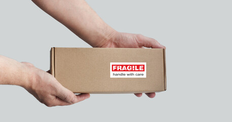 One rectangular cardboard box is held in the hands on a plain light background. A box with an...