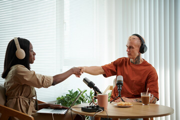 Podcaster and her guest in headphones shaking hands over table
