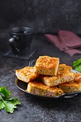 Sliced snack cake with zucchini, ham and cheese on a black plate on a dark concrete background. Recipes for zucchini.
