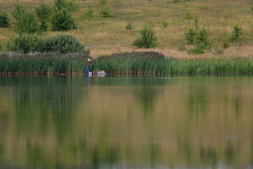nature, lake, ducks swim, a man on the opposite bank catches fish, a lot of green grass