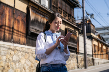 concentrated Asian chinese female visitor checking travel guide on mobile phone in the sun while visiting Gion Hanamikoji Street in Kyoto japan.