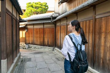rear view of asian Chinese female backpacker looking at ancient traditional wooden buildings while exploring in stone paved Gion Ishibeikoji Lane in Kyoto japan.