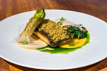 A fish fillet delicately poised atop a bed of creamy mashed potatoes, adorned with vibrant greens, presented with elegance on a tastefully arranged plate. Close-up photo. Selective focus.