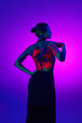 Back view. Tender posing woman in digital neon filter lights showing red flower on back over gradient purple background.