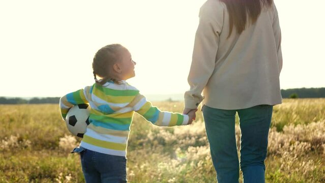 mother daughter walked hand hand, while girl happily walked alongside soccer ball. joyful smile her face, child enjoyed company mother. Together fulfilled childhood dream strolling across football