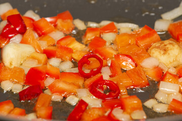 Chili peppers, bell peppers, onions and garlic are sautéed in boiling oil in a pan.